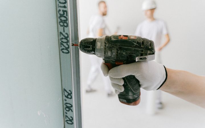 Hand driving a screw through drywall into a metal stud with a cordless drill