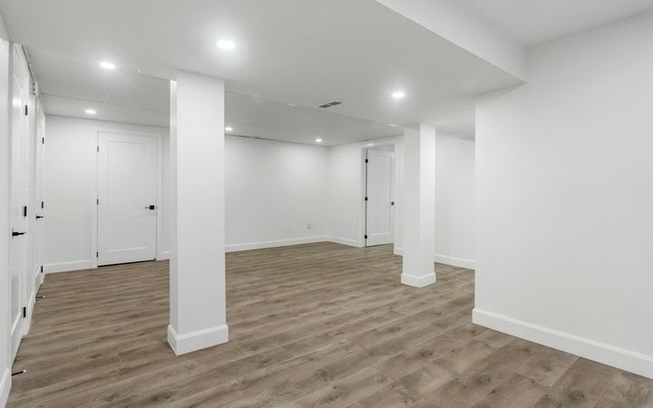 Finished basement with white walls, square posts and a vinyl plank floor
