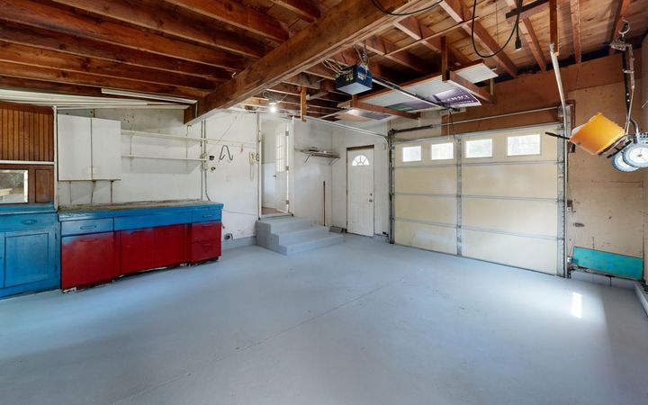 Empty garage with exposed ceiling joists, storage cabinets and an overhead door