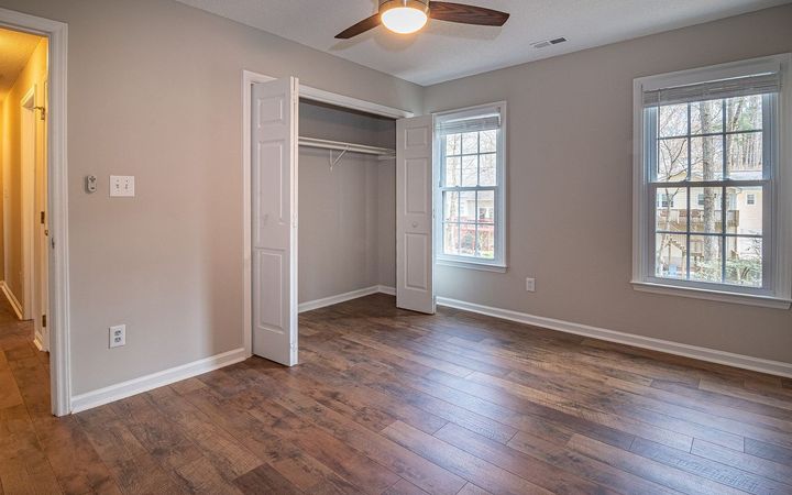 Empty bedroom with an open closet, a ceiling fan and a wood floor